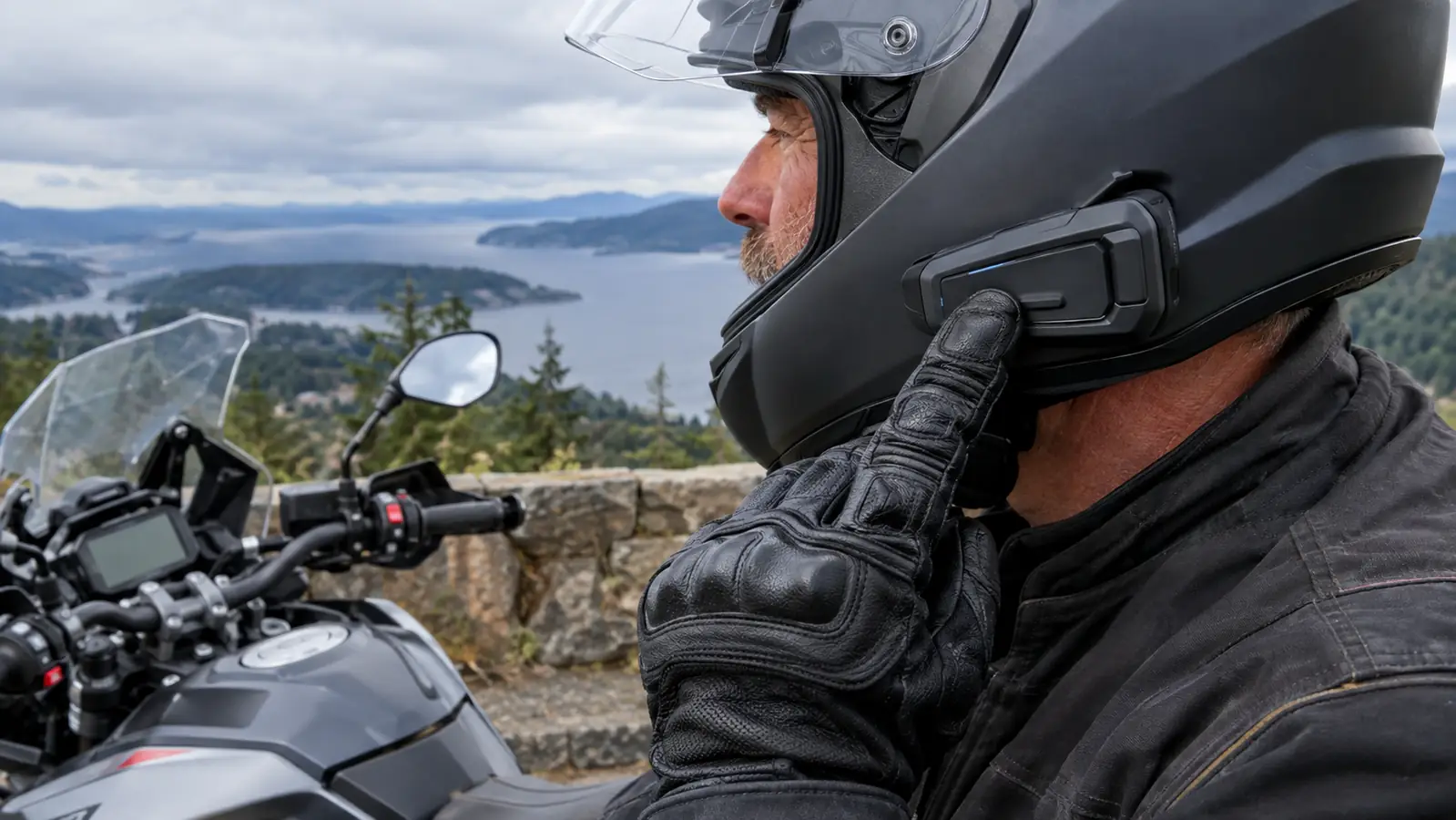 Close-up of a rider's gloved hand reaching toward a helmet-mounted intercom unit before a ride